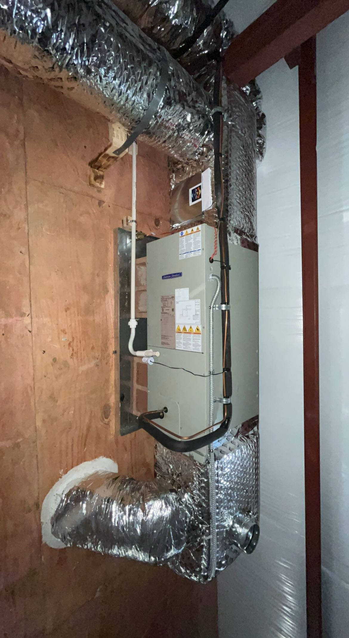 HVAC unit installed on an unfinished wall, with insulated ductwork connected and visible wiring components.